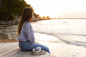 Person sitting peacefully by the sea, looking out at the water