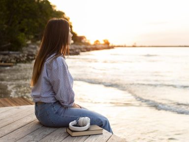 Person sitting peacefully by the sea, looking out at the water